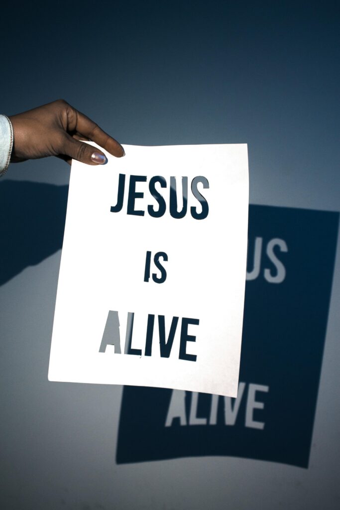 A hand holding a sign that says Jesus is Alive.