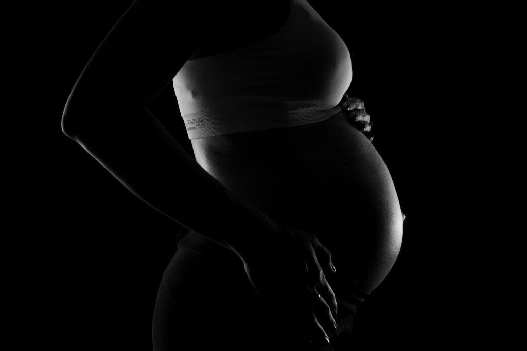 A black and white image of a woman with a large pregnant belly being held by her hands.