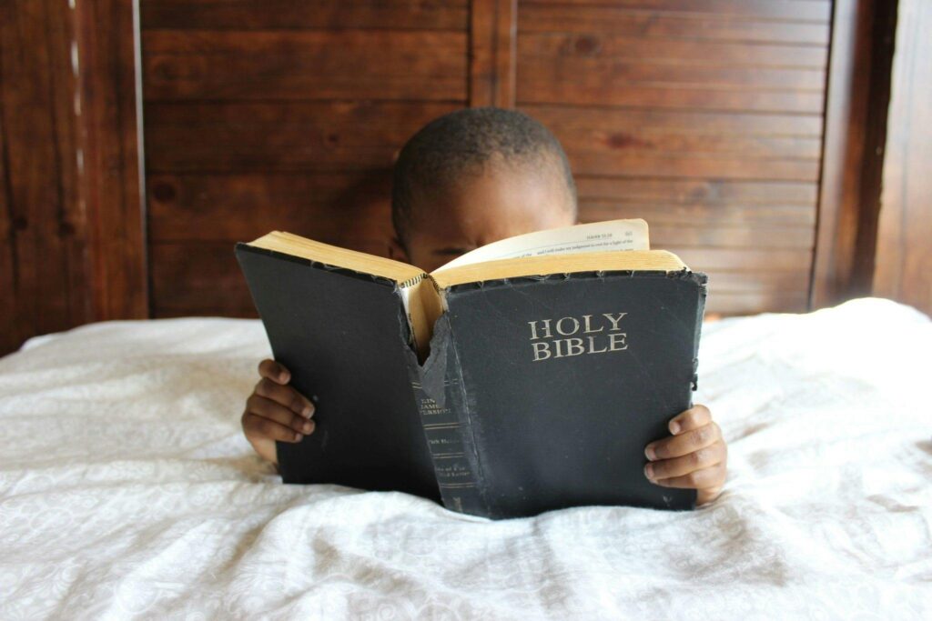 Image of young boy sitting in bed holding and reading the bible.