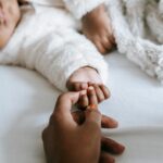 Image of a woman and baby hand touching each other while laying down on a bed.