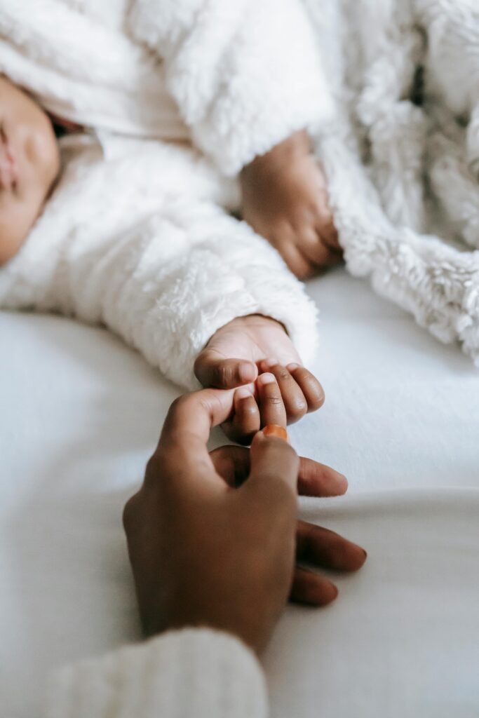 Image of a woman and baby hand touching each other while laying down on a bed.