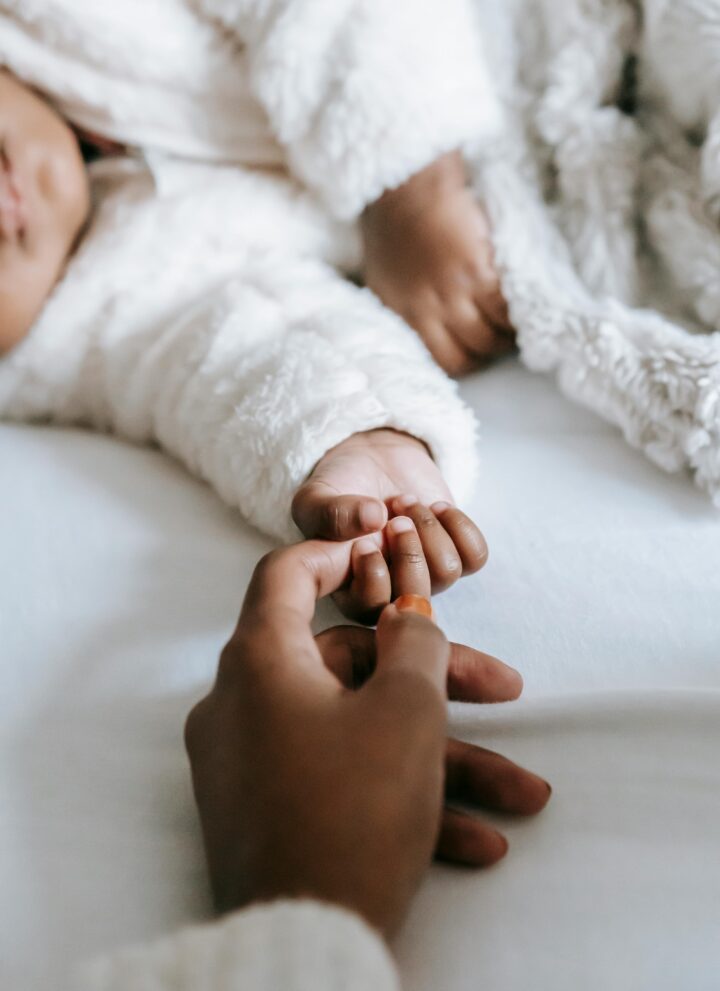 Image of a woman and baby hand touching each other while laying down on a bed.