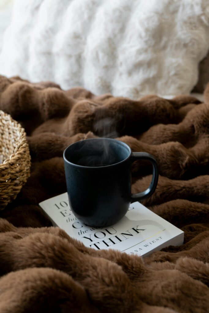 An image of a mug on a cook atop a brown comforter on a bed.