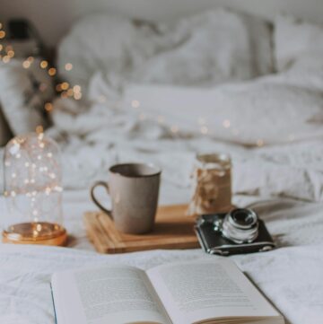 An image of a mug on a bed with an open book and flowers.