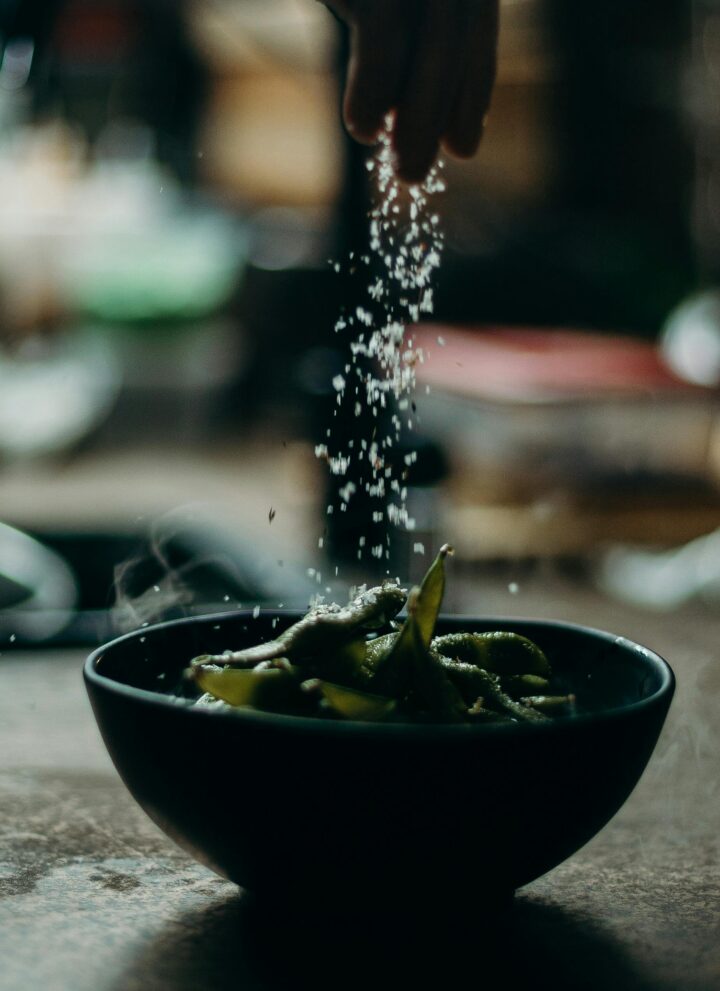 Image of coarse salt being sprinkled with hands over food in a bowl.