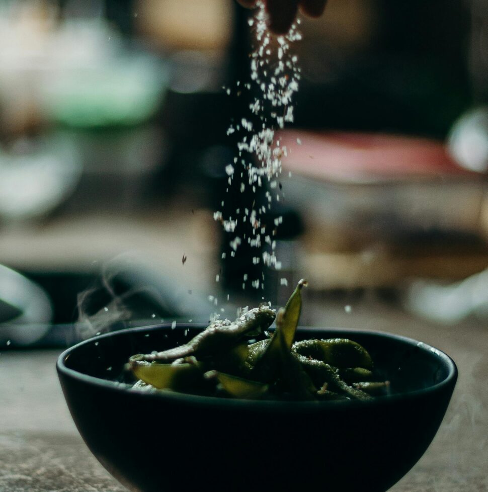 Image of coarse salt being sprinkled with hands over food in a bowl.