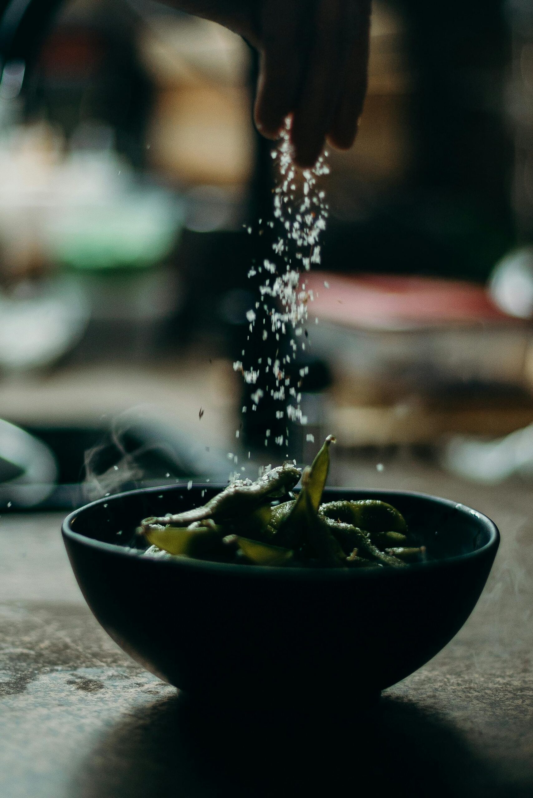 Image of coarse salt being sprinkled with hands over food in a bowl.