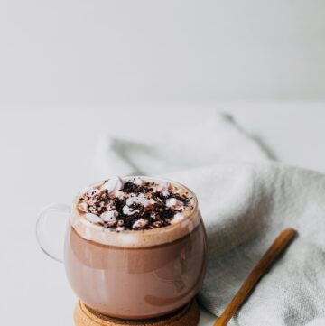 An image of a mug with hot chocolate with a spoon on a white table.