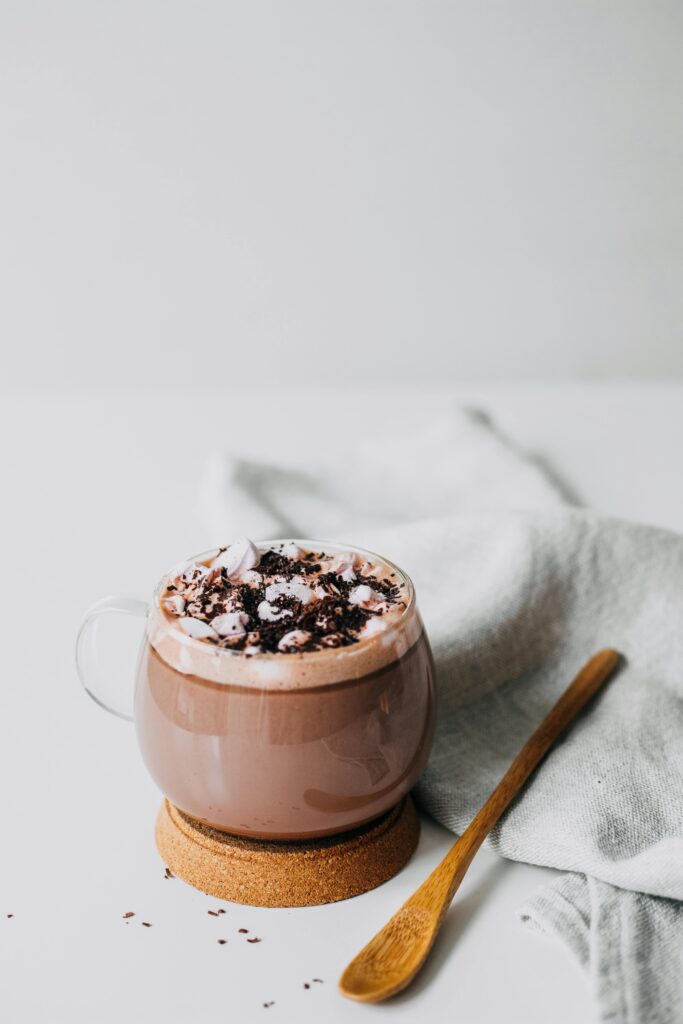 An image of a mug with hot chocolate with a spoon on a white table.