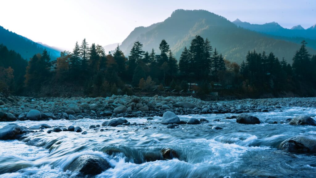 Image of mountains, trees, and water with rocks.